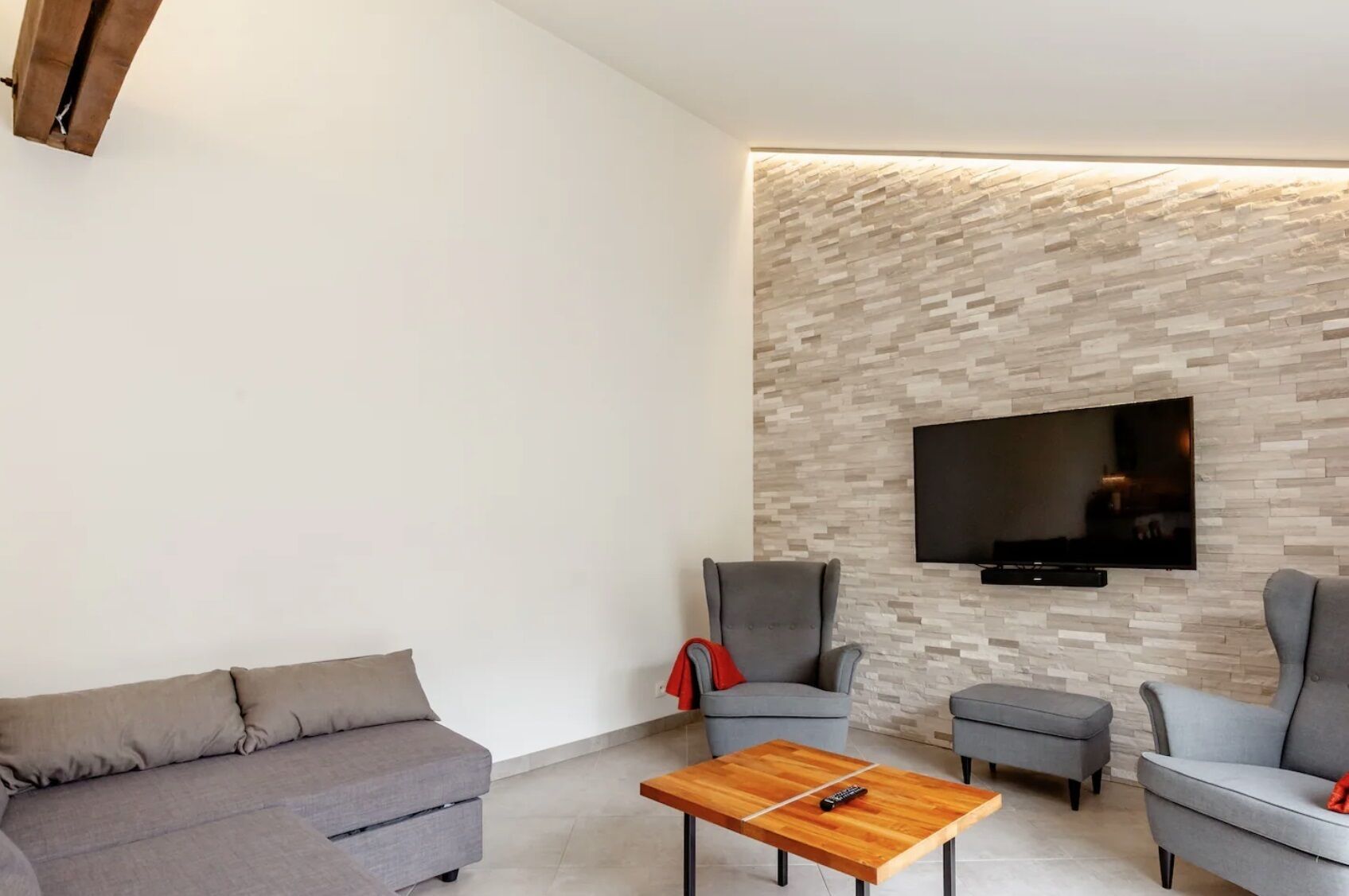Una sala de estar moderna con un sofá gris, dos sillones, una mesita de centro y un televisor de pantalla plana montado en una pared con textura.