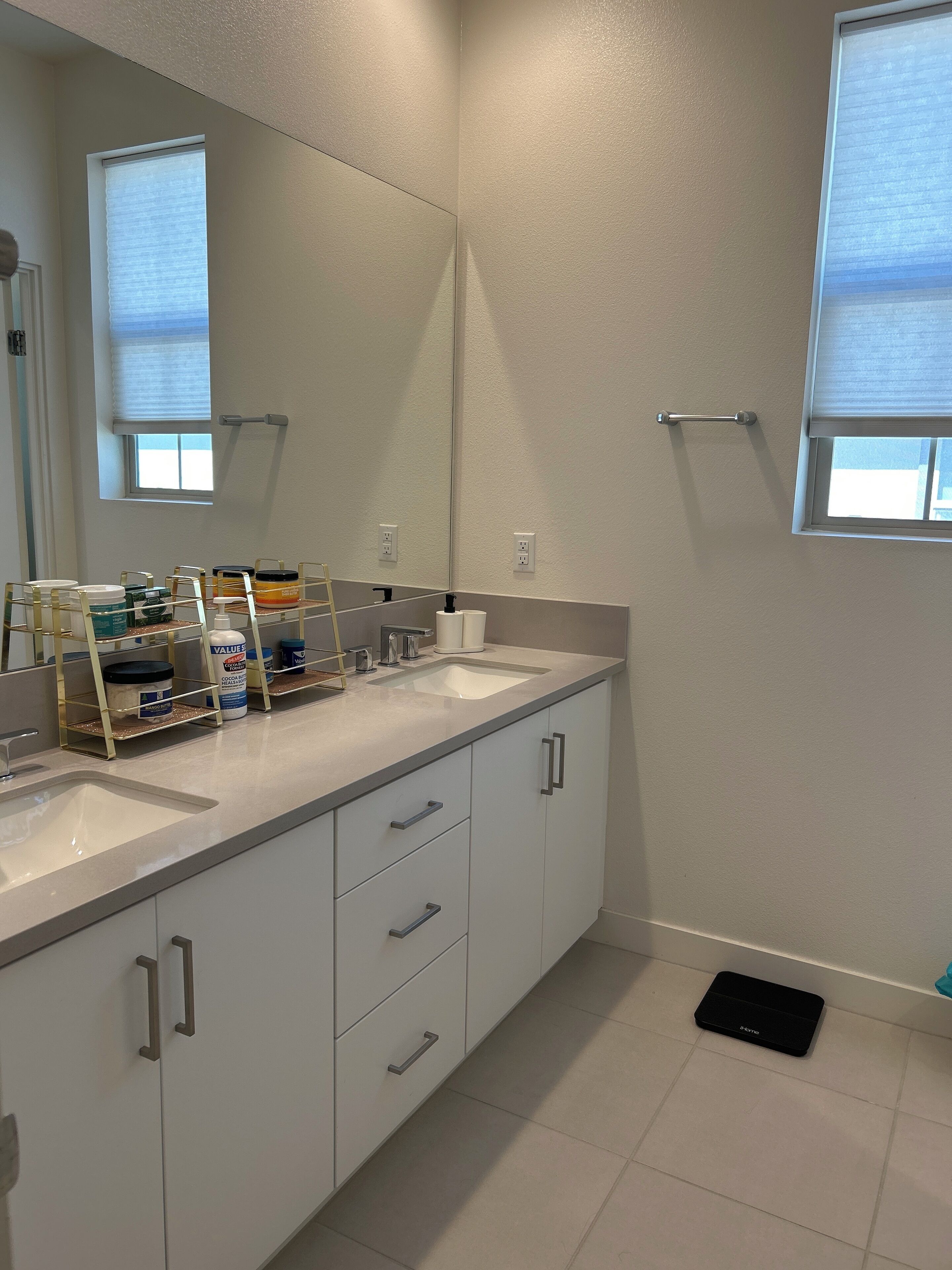 A modern bathroom with two sinks, a large mirror, and a window with blinds.