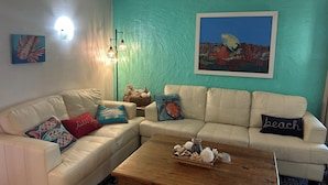En stue med teal farvede vægge, en hvid sofa og et træbord.