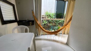A clean, modern room with a white table and chairs, a hammock, and a view of greenery through a sliding glass door.