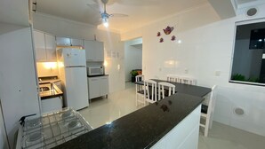 A modern kitchen with white cabinets, a black countertop, a gas stove, a microwave, and a ceiling fan.