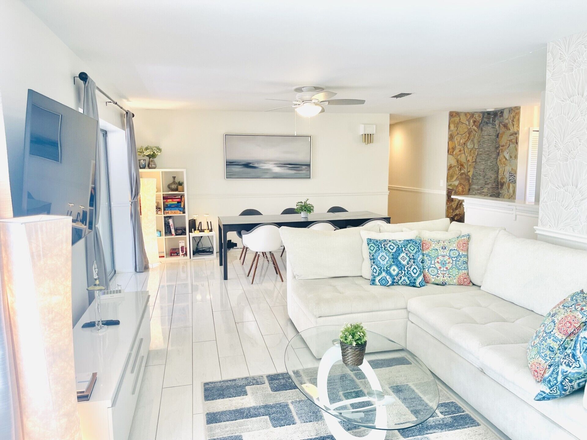 Uma sala de estar moderna com um sofá branco, uma mesa de centro de vidro e uma área de jantar com mesa e cadeiras.