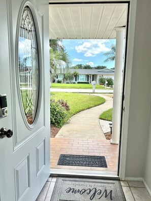 A residential entrance with a white door, a welcome mat, and a clear view of a well-maintained lawn and pathway leading to a house.