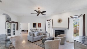 A spacious living room with a fireplace, a ceiling fan, and a large window. - Luxury home NW Bradenton Fl (Bradenton)