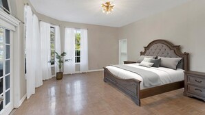 A bedroom with a large bed, a nightstand, a potted plant, and a ceiling light fixture. - Luxury home NW Bradenton Fl (Bradenton)