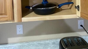 A wooden cabinet with three black pans with blue handles, a power outlet, and a toaster on the countertop. - Cozy New Apartment in Fairbanks (Fairbanks)