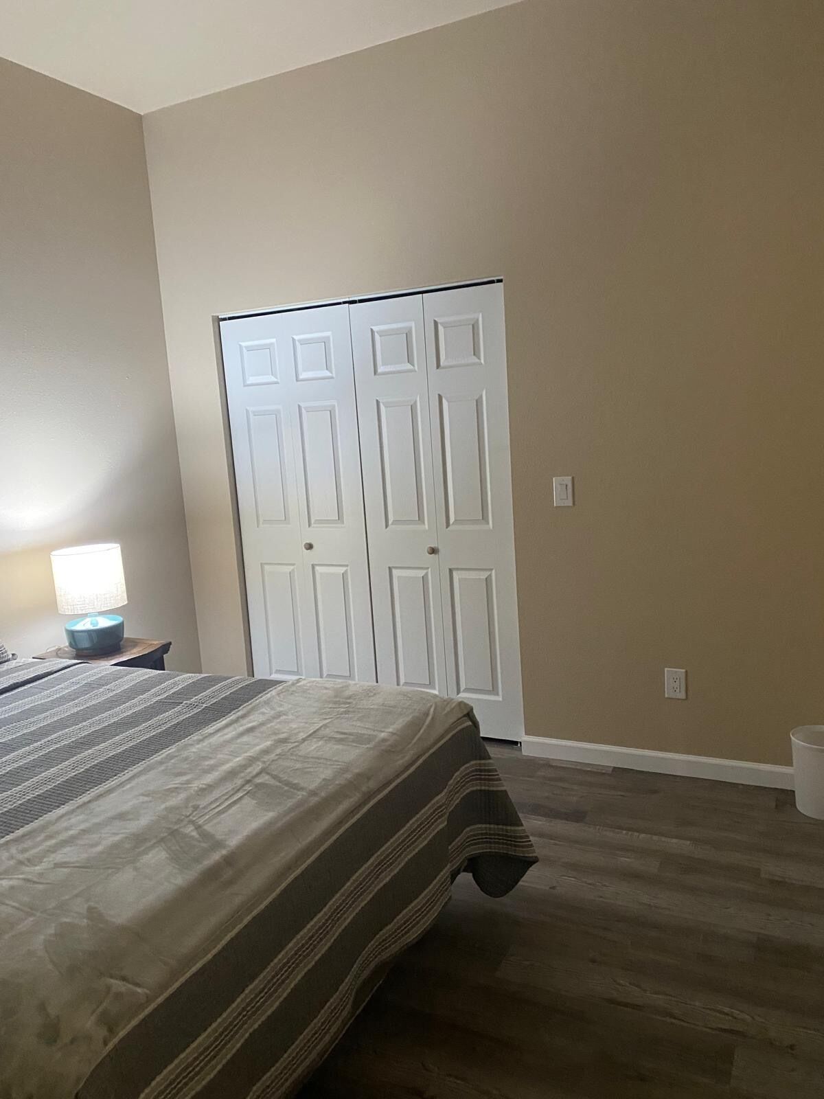 A bedroom with a bed, a nightstand, a lamp, and a closet.