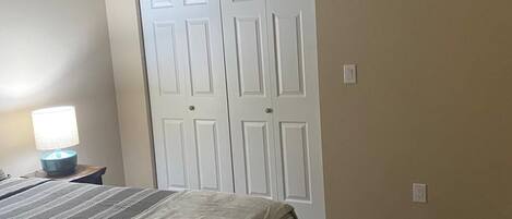 A bedroom with a bed, a nightstand, a lamp, and a closet.