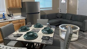 A compact living space with a kitchenette, a dining table set with green plates, a gray sofa, and a round coffee table. - Cozy New Apartment in Fairbanks (Fairbanks)
