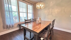 A dining area with a wooden table, chairs, a chandelier, and large windows with curtains. - Spacious 3BR Auburn Getaway – Family-Ready and Near All Auburn Has to Offer (Auburn)