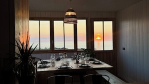 A dining area with a table set for four, large windows, and a hanging light fixture.