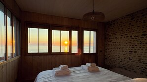 A room with a large bed, wooden walls, and a view of the sunset over the sea.