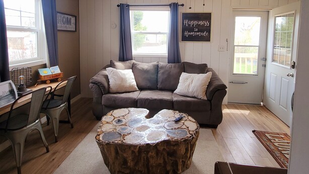 A cozy living room with a brown sectional sofa, a wooden coffee table, a desk with a chair, and a ceiling fan. - Comfortable and Cozy 1-bedroom house in delightful Rapid City with AC & Wifi (Rapid City)
