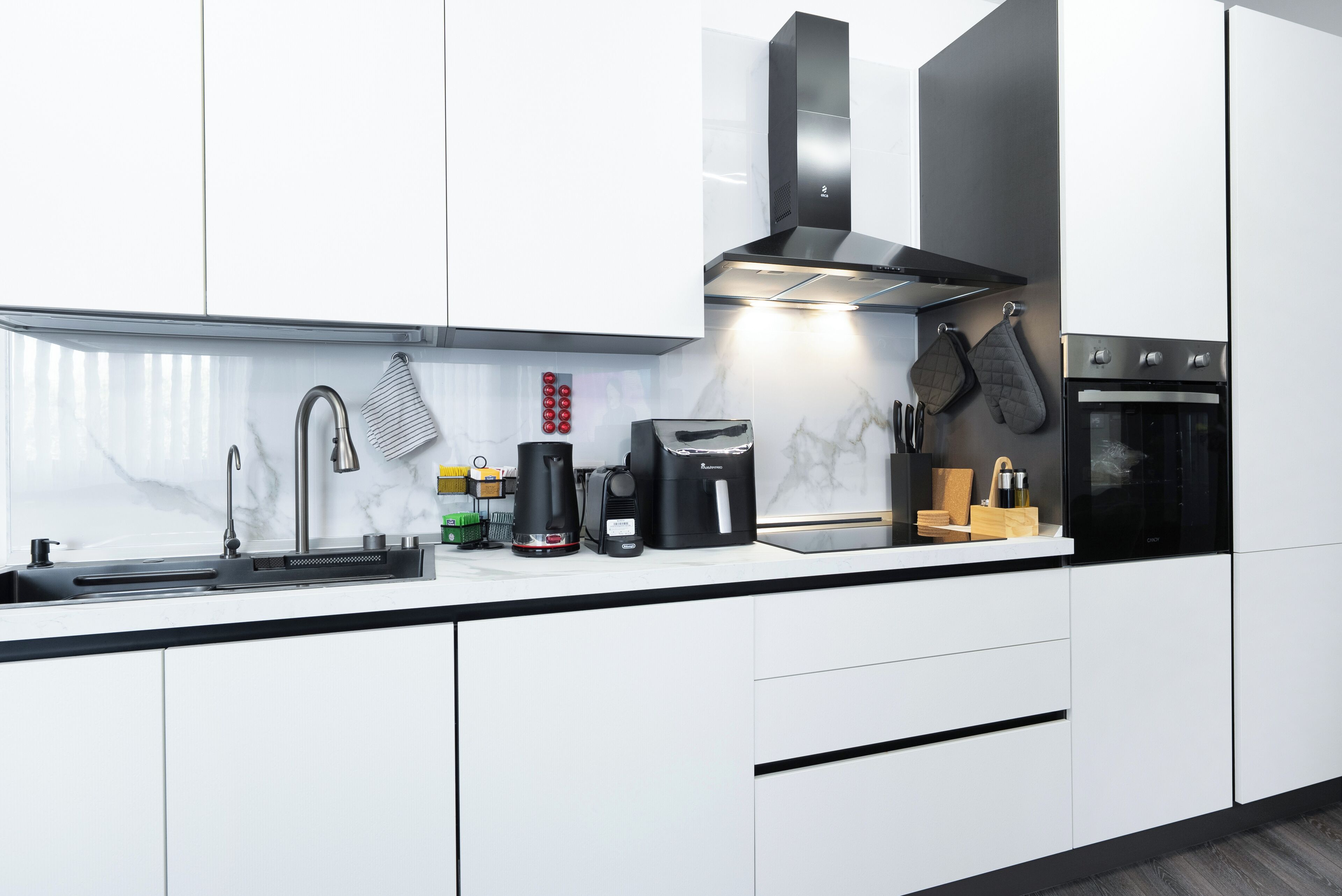 A modern kitchen with white cabinets, a stainless steel sink, a coffee maker, and a built-in oven.