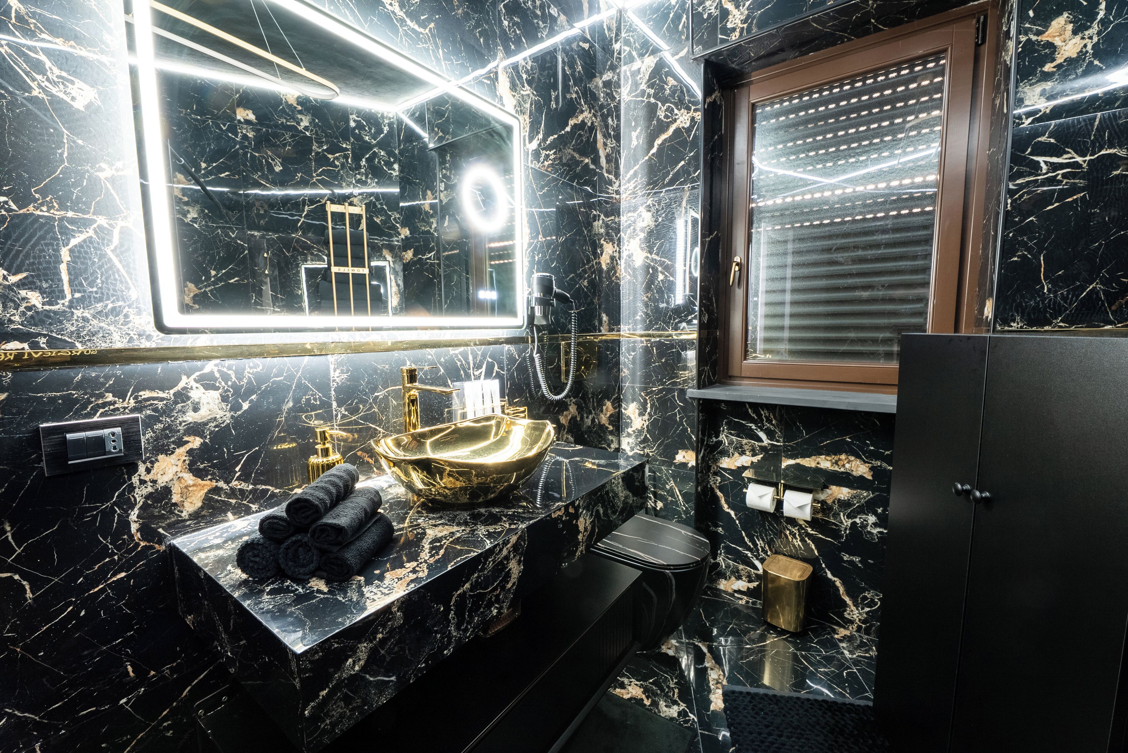 Ein modernes Badezimmer mit einem schwarzen Marmorwaschbecken, goldenen Armaturen und einem großen Spiegel mit LED-Beleuchtung.