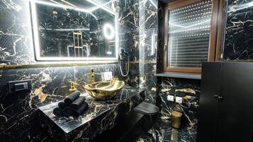 Ein modernes Badezimmer mit einem schwarzen Marmorwaschbecken, goldenen Armaturen und einem großen Spiegel mit LED-Beleuchtung.
