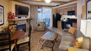 A cozy living room with a fireplace, a dining table, a sofa, and a kitchen area with a microwave and refrigerator.