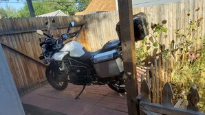 A motorcycle parked in a covered outdoor area with a wooden fence and a brick floor. - Charming 1-bedroom private apartment in a cottage with AC & WiFi (Colorado Springs)