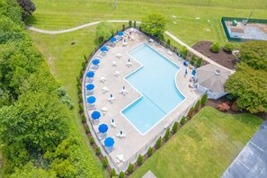 An aerial view of a swimming pool with lounge chairs and umbrellas, surrounded by well-maintained lawns and trees.