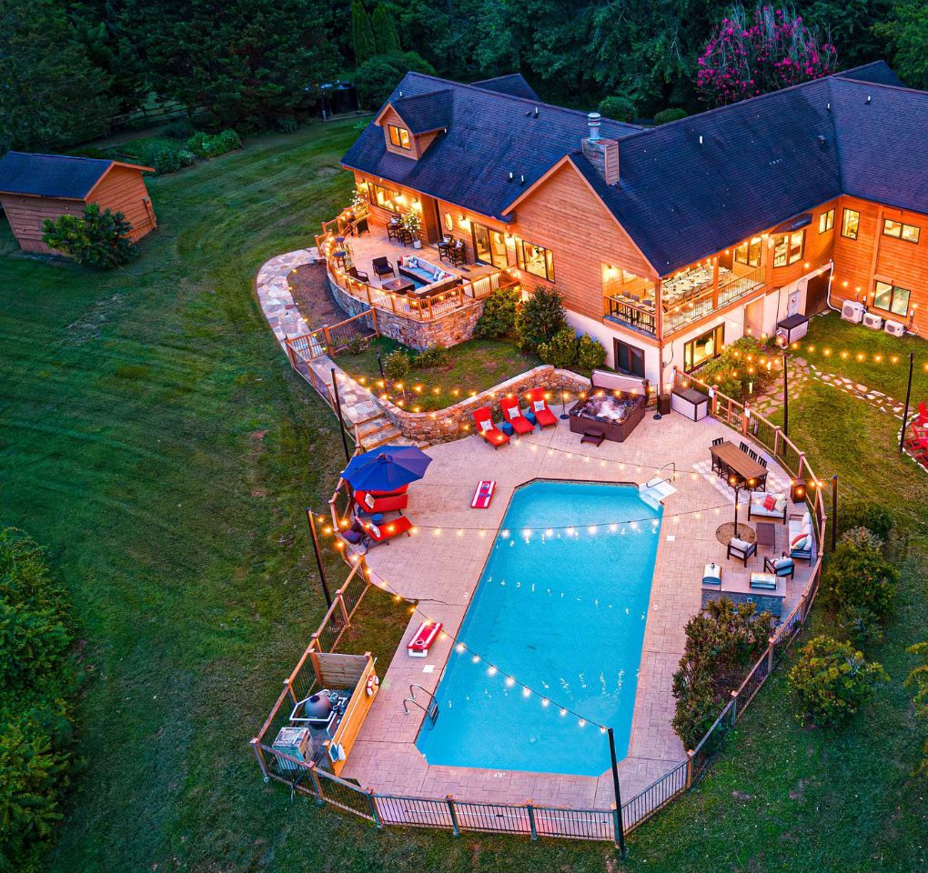Une grande maison dotée d’une piscine intérieure et d’une piscine extérieure, entourée d’une pelouse bien entretenue et d’une terrasse.
