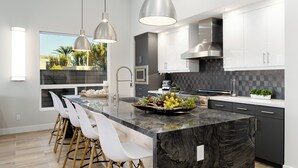 Cocina moderna con una isla grande, iluminación colgante y vistas a palmeras.