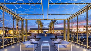 Un área de estar al aire libre con sillones blancos y mesas, rodeada por una estructura de vidrio geométrico.