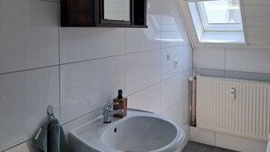 Ein Badezimmer mit einem weißen Waschbecken, einem Holzschrank, einem Spiegel und einem Oberlicht.