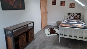 Ein Schlafzimmer mit einem Bett, einem Holzschrank, einem Kuhfellteppich und einer Deckenleuchte.