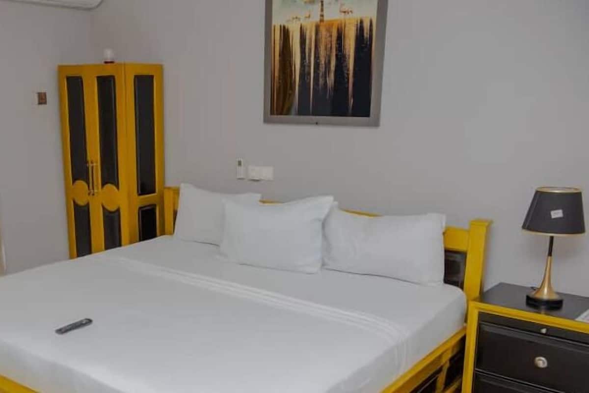 A hotel room with a bed, a nightstand, a lamp, a wardrobe, and a painting on the wall.