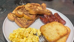 Une assiette de petit-déjeuner avec des toasts, des saucisses, des œufs brouillés et un verre de jus d’orange.
