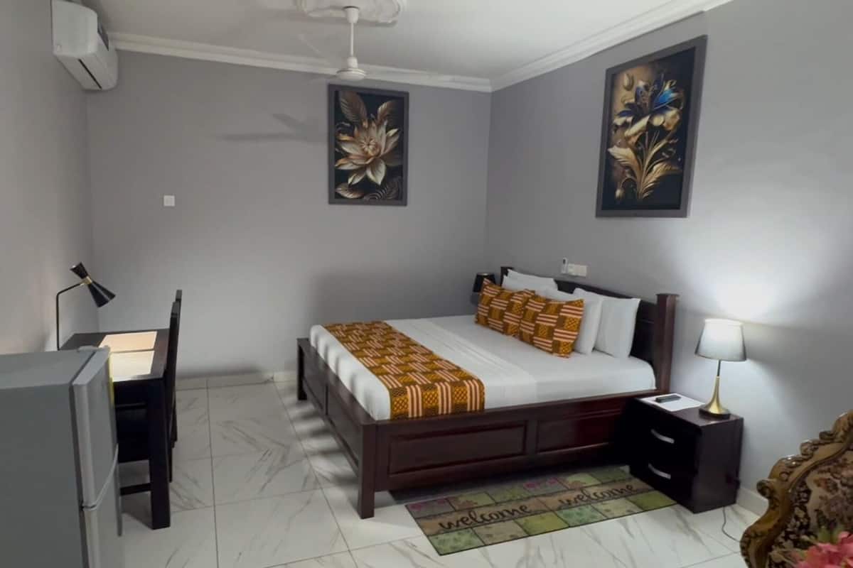 A bedroom with a bed, desk, chair, nightstand, and two wall-mounted paintings.