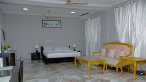 Une chambre d’hôtel avec un lit, un canapé, une table basse, un ventilateur de plafond et un tableau au mur.