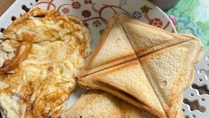 Une assiette avec une omelette grillée et des tranches de pain grillé, une tasse avec une cuillère, et un plateau à motifs floraux sur une table en bois.
