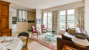 Een moderne woonkamer met een glazen salontafel, twee roze fauteuils, een bruine bank en een eethoek met een houten kast en een tafel gedekt voor twee personen.