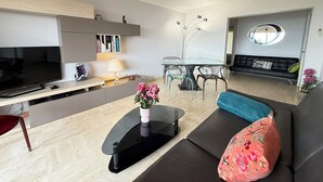A modern living room with a flat-screen TV, a glass dining table, a sofa, and a black leather couch.