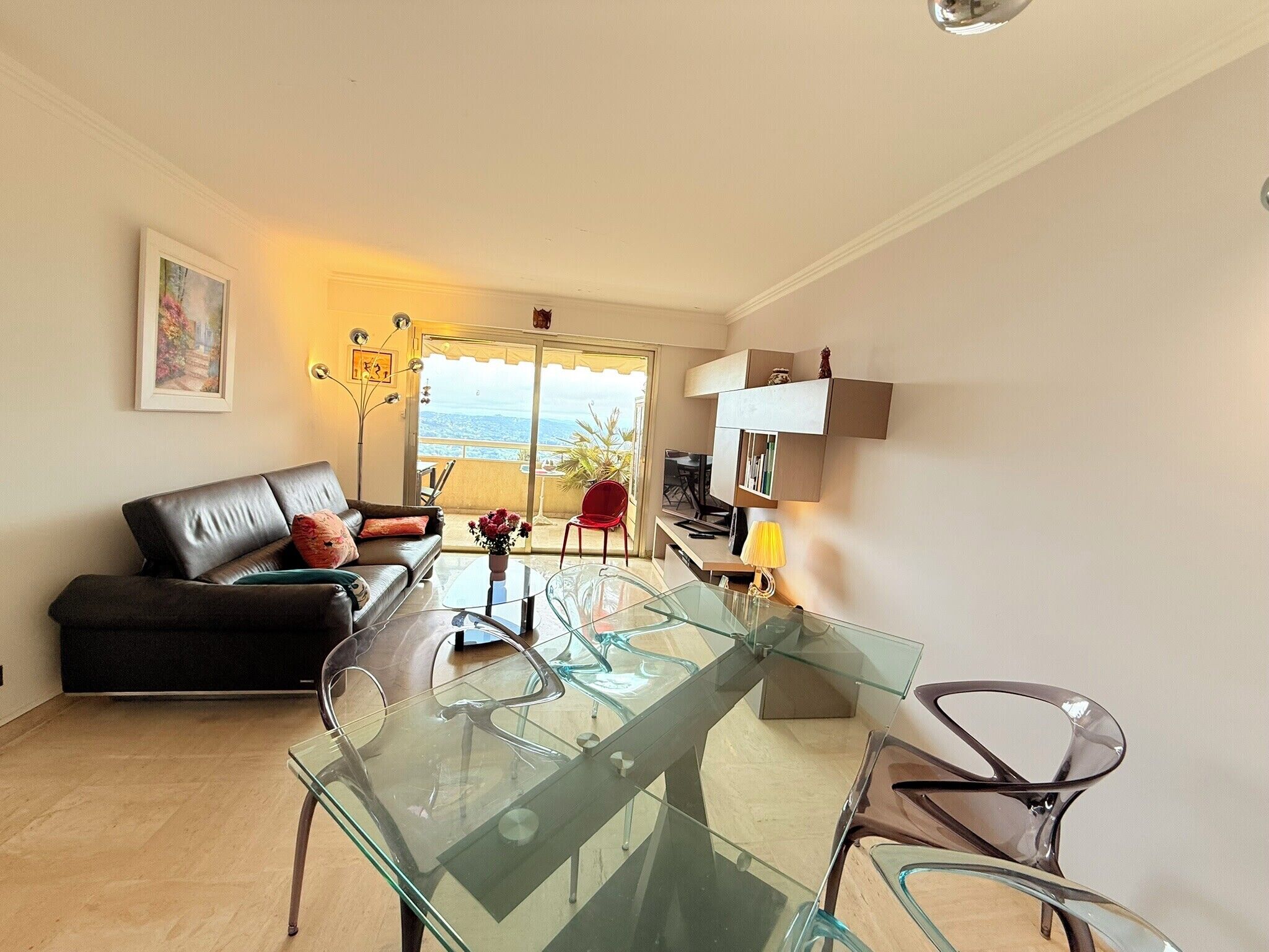 Un salon moderne avec une table basse en verre, un canapé en cuir noir et un coin repas agrémenté d’une chaise rouge.