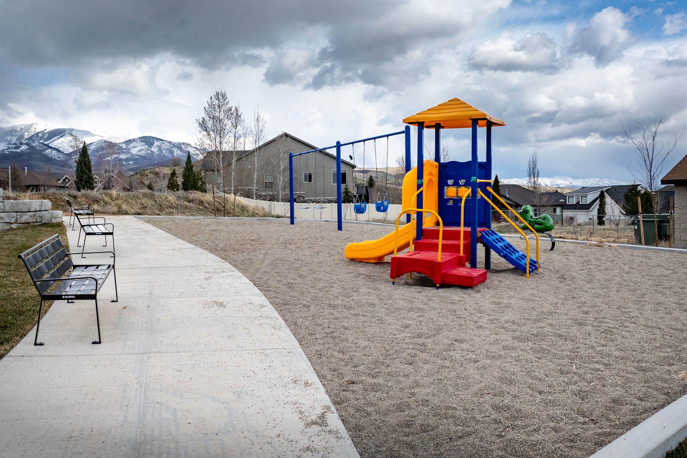 A playground with a slide and climbing structures, a bench, and a paved walkway.