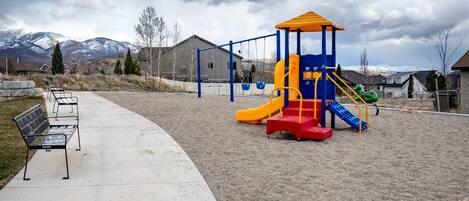 A playground with a slide and climbing structures, a bench, and a paved walkway.