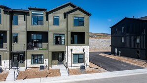 A modern multi-story residential building with a stone facade, large windows, and a well-maintained driveway. - Bear Cub’s Den R5983 | Snowbasin Ski Escape | EV (Mountain Green)