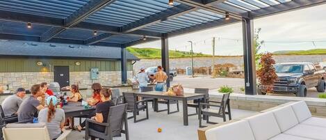Un patio al aire libre con mesas y sillas, una parrilla y una zona de estar cubierta.