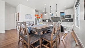 A modern kitchen with white cabinets, a wooden dining table, and a hanging light fixture. - Bear Cub’s Den R5983 | Snowbasin Ski Escape | EV (Mountain Green)
