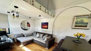En moderne stue med en modulsofa, et spisebord med stole, trægulv og en loftlampe.