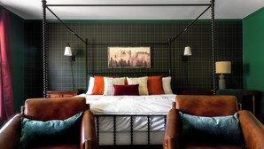 Une chambre à coucher avec un lit, deux fauteuils, un tableau au mur et deux lampes de chevet.