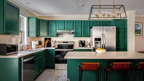 Une cuisine avec des meubles de couleur verte, des appareils en acier inoxydable et un îlot central doté de chaises.