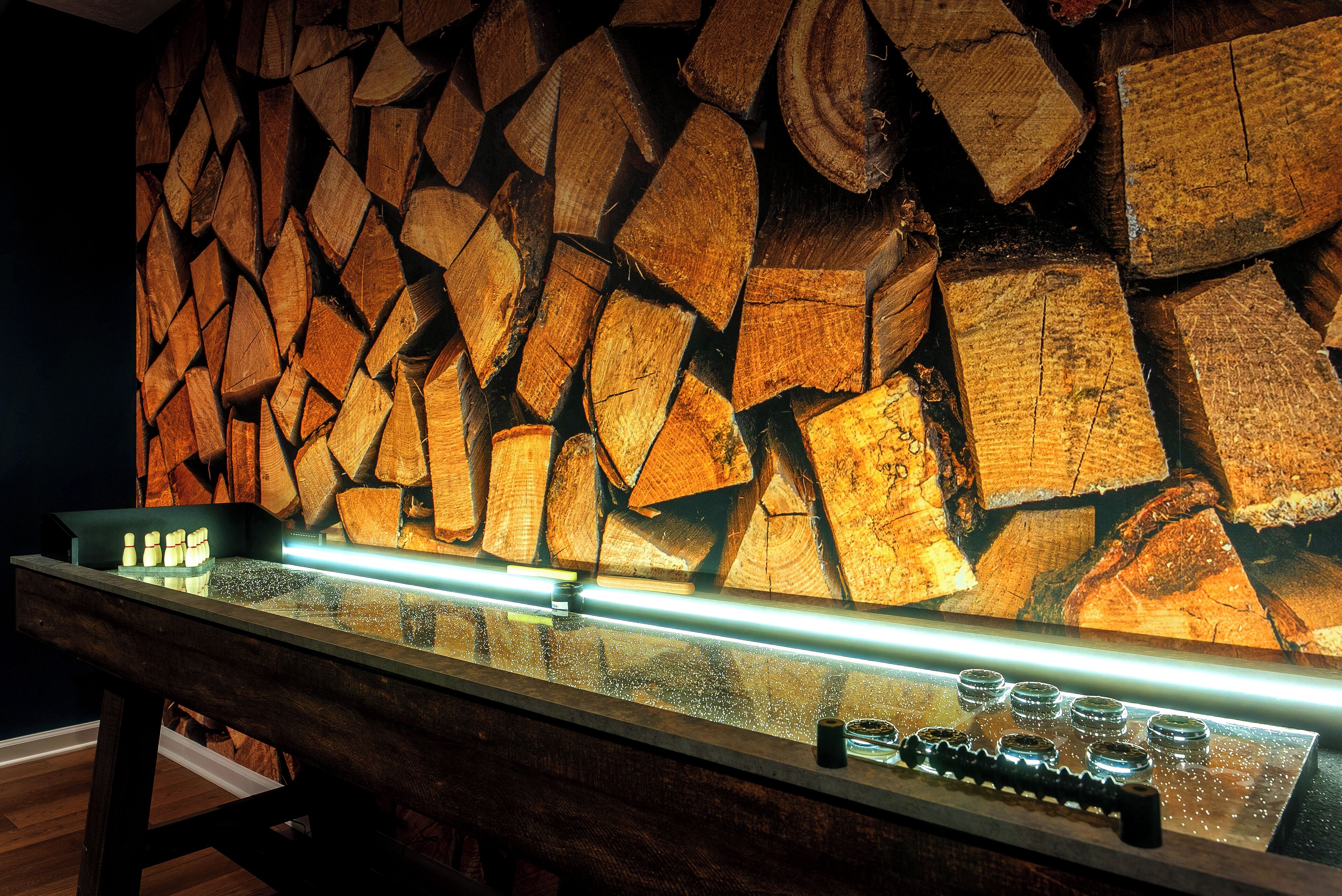 Pared de madera con leña apilada y una vitrina de vidrio con botellas.