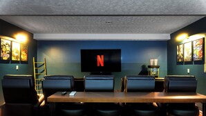 Une pièce dotée d’un grand téléviseur à écran plat fixé au mur, d’une table en bois et de six chaises en cuir noir.
