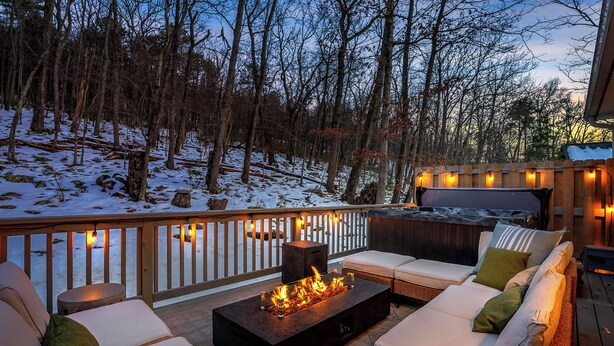 Une terrasse avec des sièges extérieurs et un foyer, entourée d’un paysage enneigé et d’arbres.