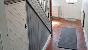 Un escalier avec des rampes blanches et une main courante en bois, menant à une porte dotée d’une fenêtre.
