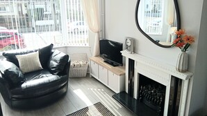 Un salon avec un canapé en cuir noir, un téléviseur à écran plat, une cheminée et un grand miroir.