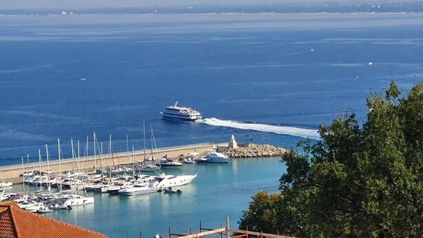 A marina with numerous boats docked, a clear view of the sea, and a distant ship creating a wake. - LODGE ROSA In the pearl of Cilento, cozy studio apartment, Trentova Bay. (Agropoli)